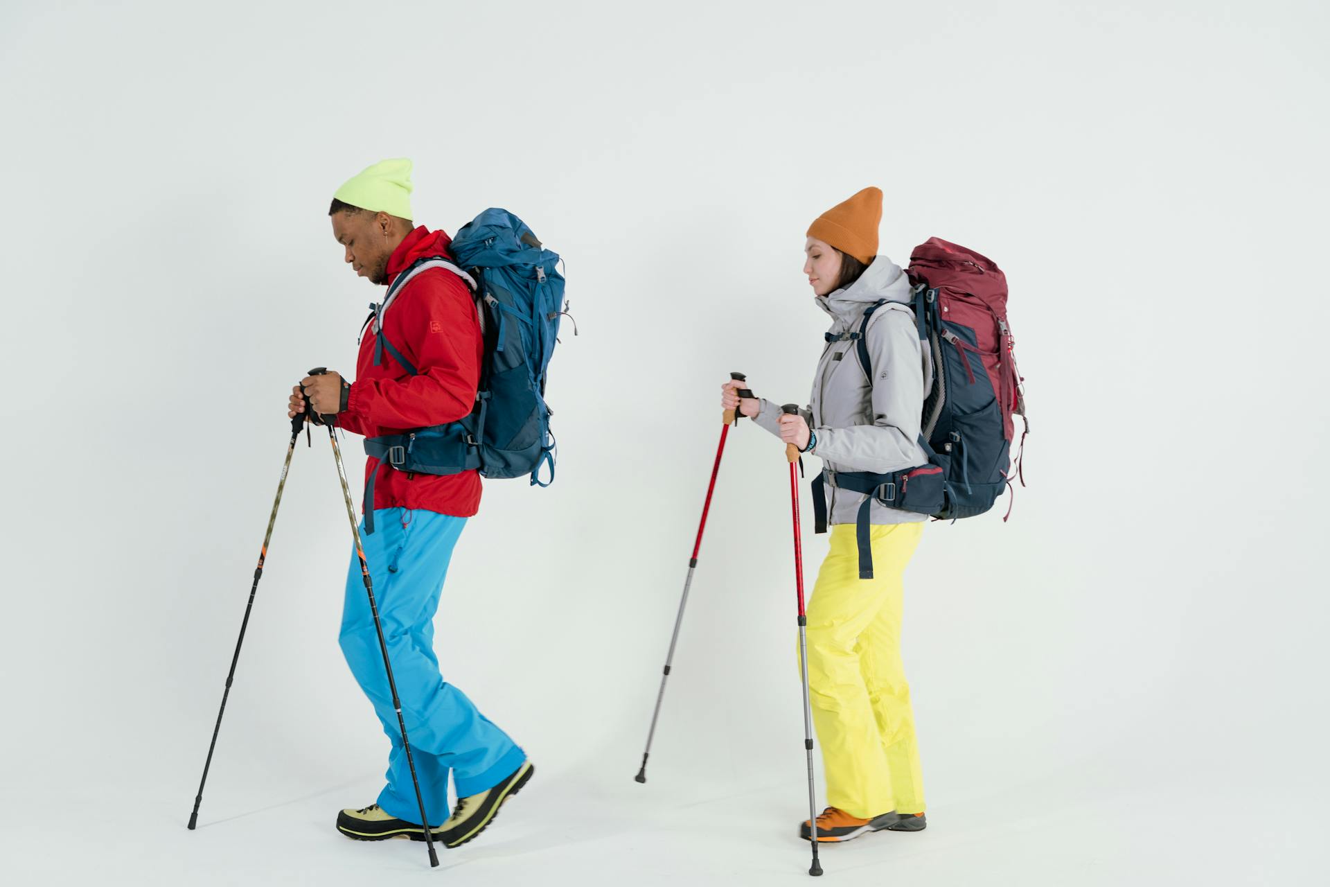 Two hikers in colorful winter gear with trekking poles, ready for an indoor photo shoot.