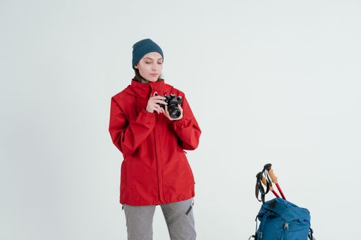 Young woman in winter hiking outfit holding a camera, standing in a studio setting with backpack.