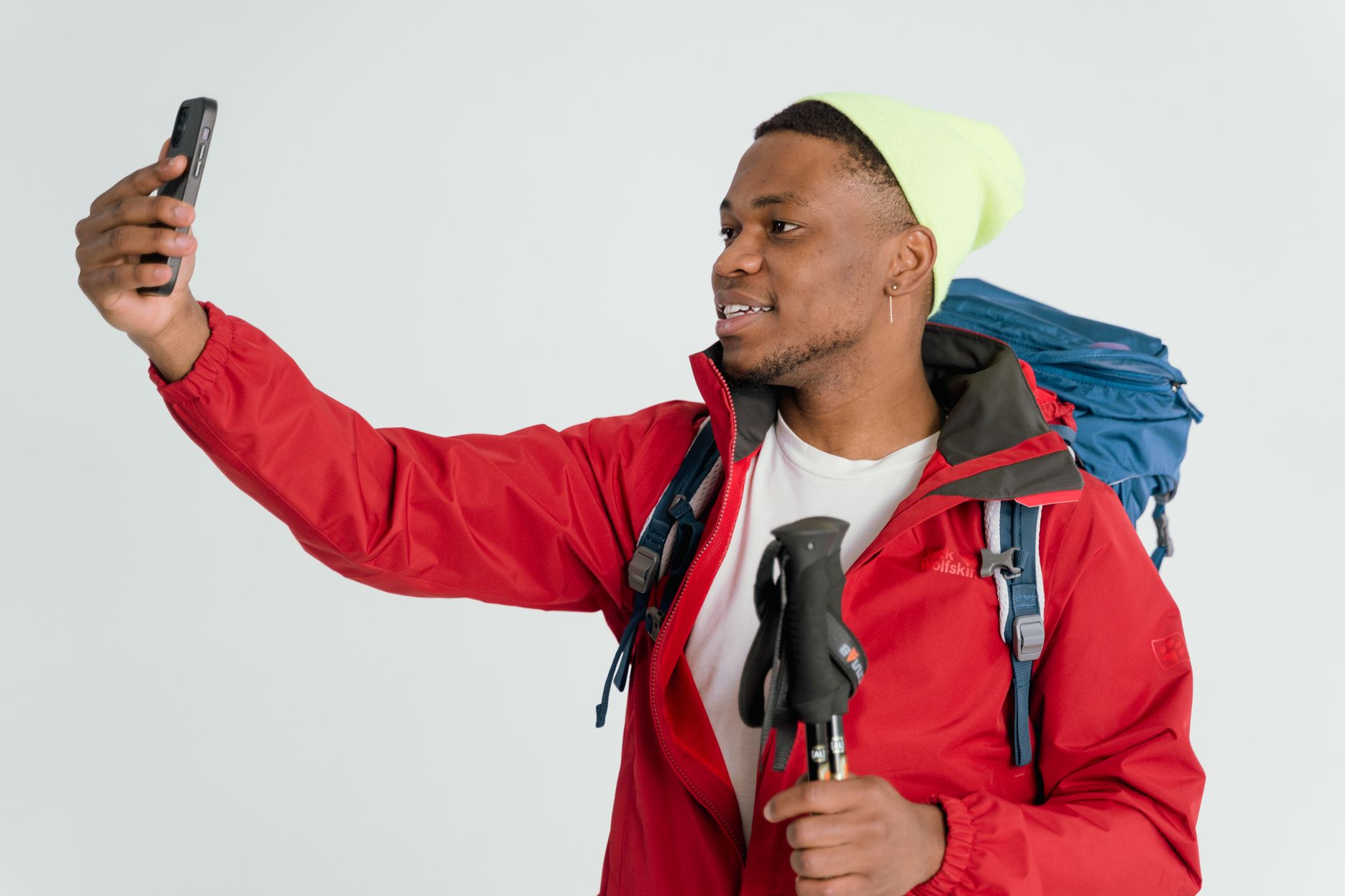 Smiling young man in hiking gear taking a selfie indoors against a white background.