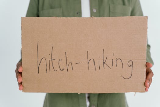 Close-up of a person holding a handmade hitchhiking sign on cardboard.