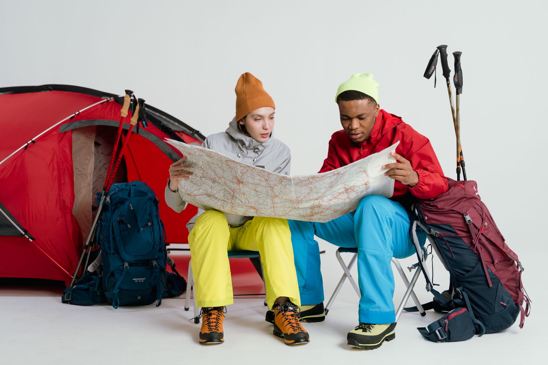 Two travelers planning an adventure trip, examining a map with camping gear.