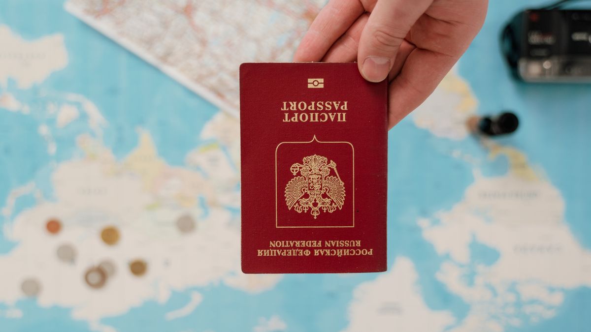 A hand holding a Russian passport over a map, suggesting travel preparation.