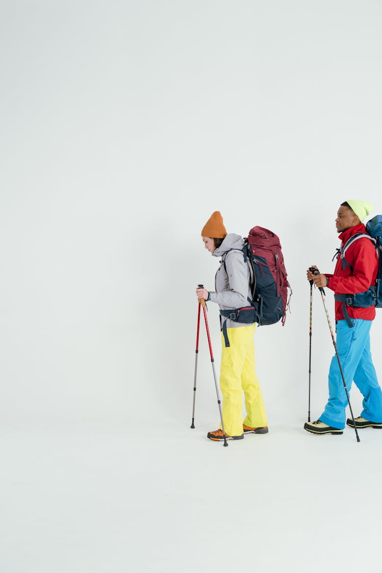 A Man And. Woman With Back Packs Walking With Trekking Poles 