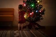 一个年轻女孩穿着节日礼服，在室内看着一棵装饰好的圣诞树