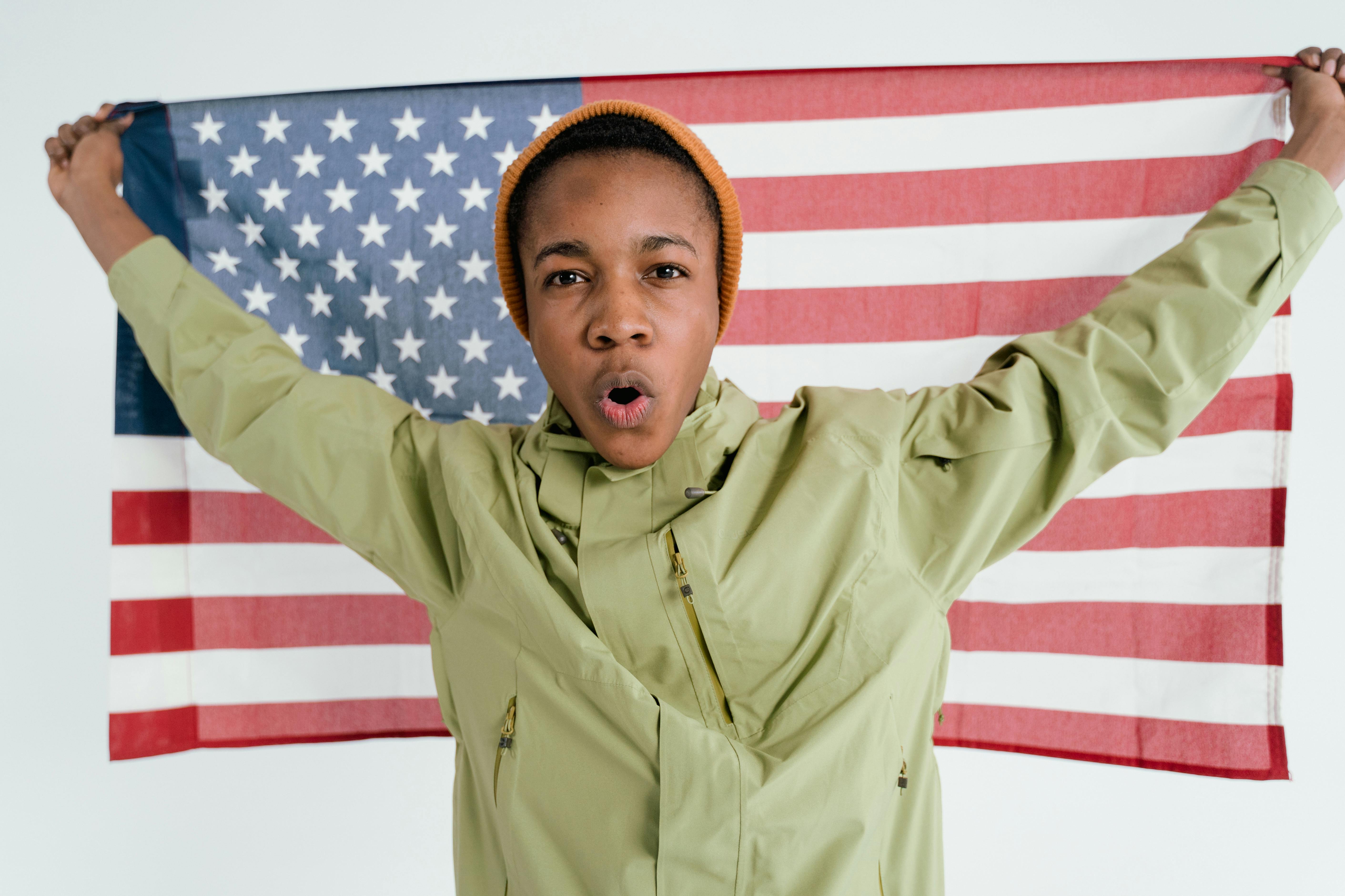 A young man energetically holds up the American flag, expressing a sense of patriotism and confidence.