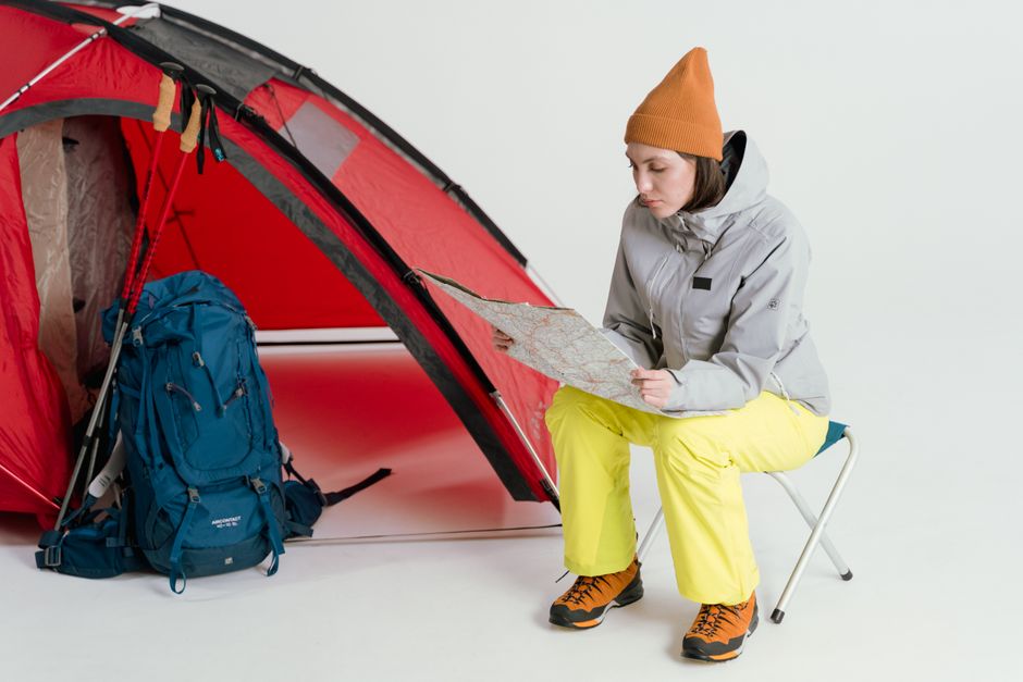 冬の服装をした女性が、屋内のキャンプテントの横で地図を研究しています。