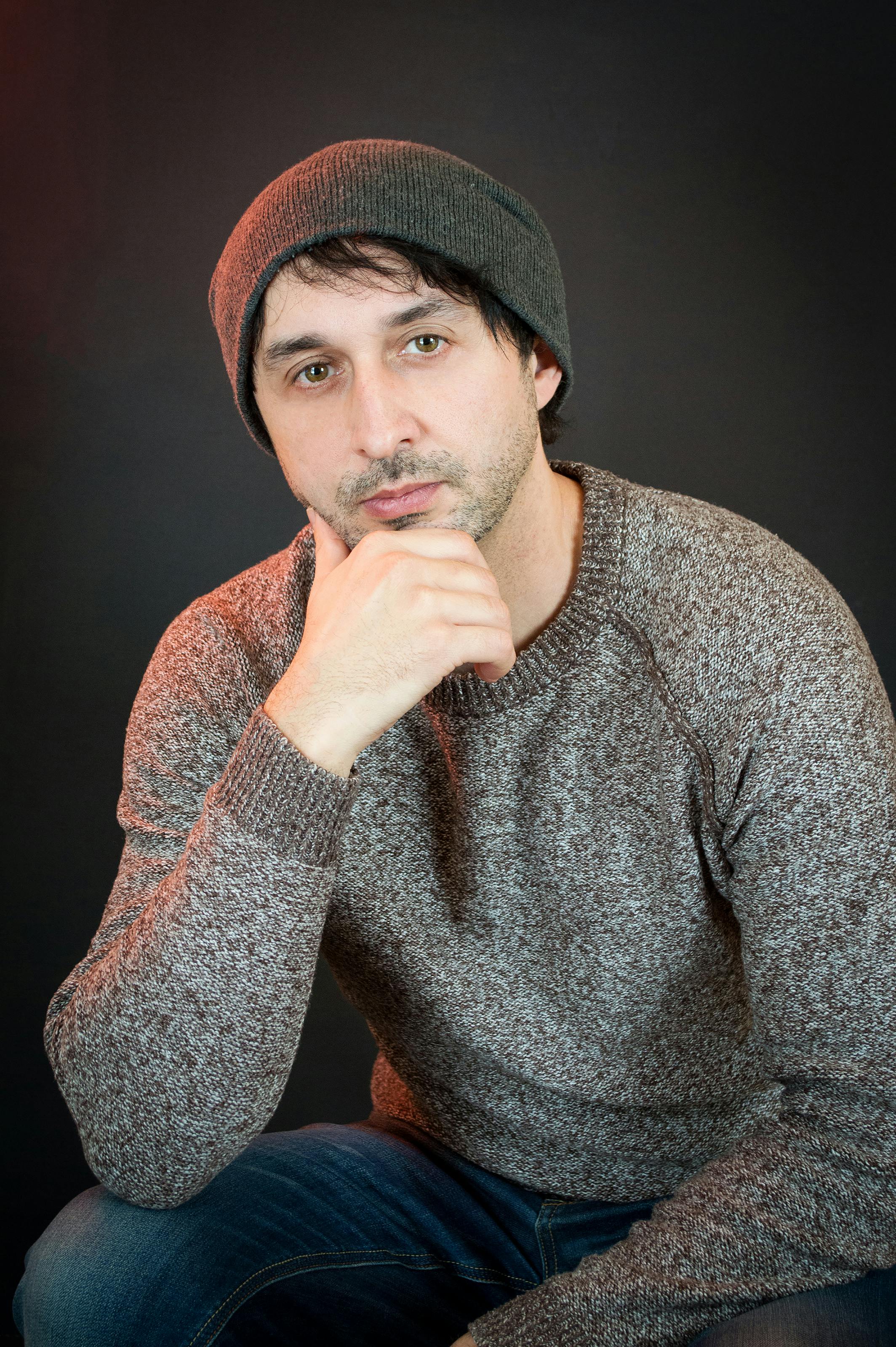 Adult unshaven male in warm clothes touching chin while leaning on hands and looking at camera