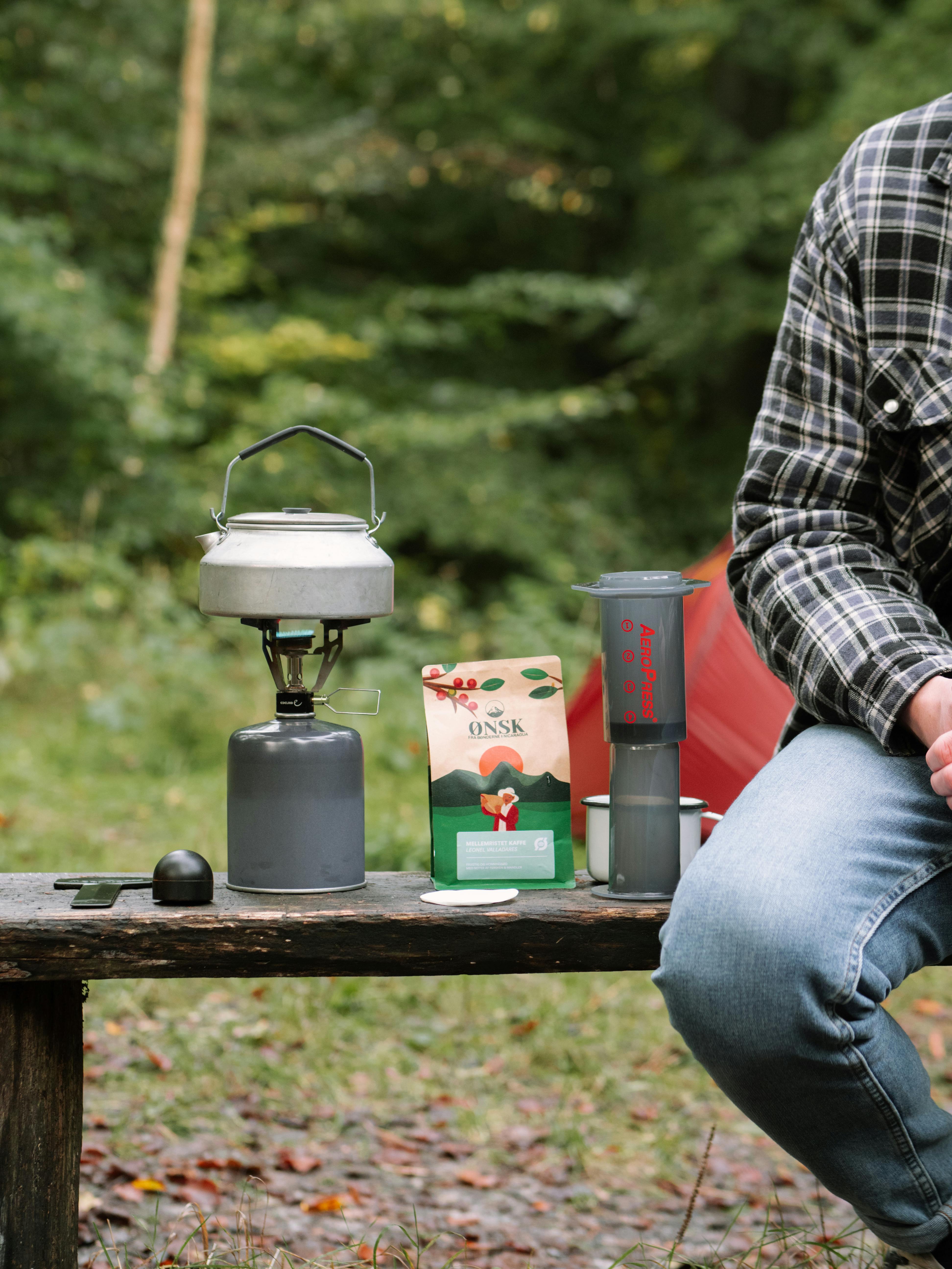 A serene outdoor setting featuring a portable coffee setup with Aeropress and camping gear.