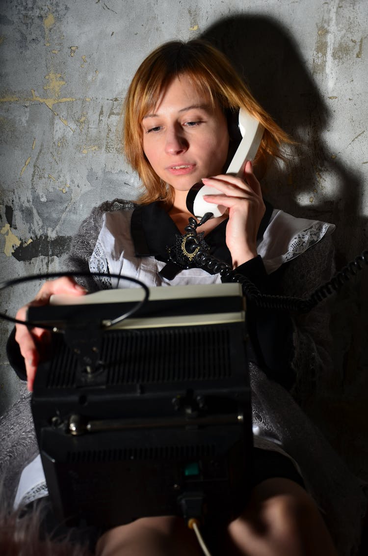 Woman Speaking On Retro Telephone Against Rough Wall