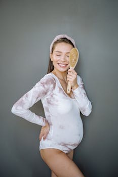 Joyful pregnant woman with a brush smiling indoors, embracing motherhood.