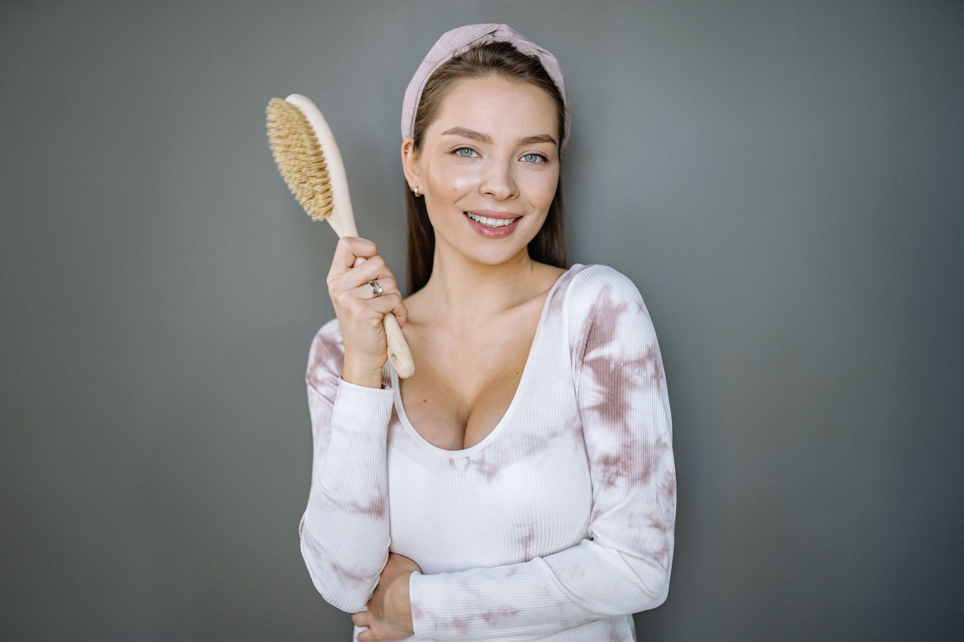 Smiling woman with long hair holding a brush, expressing joy and confidence indoors.