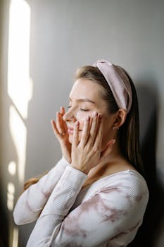 Woman enjoying a calming skincare routine by window light.
