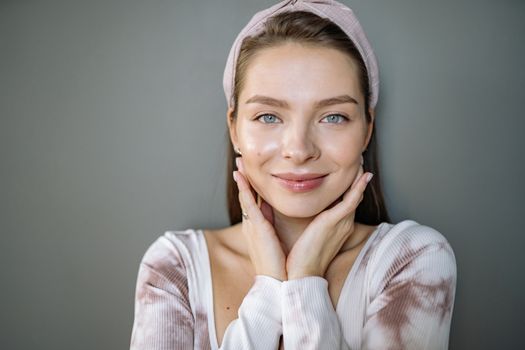 Portrait of a smiling woman with healthy skin wearing a headband on a gray background.