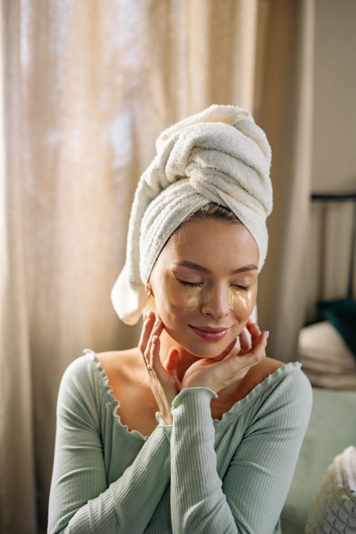 Free Serene woman with under eye patches and towel on head enjoying skincare routine. Stock Photo