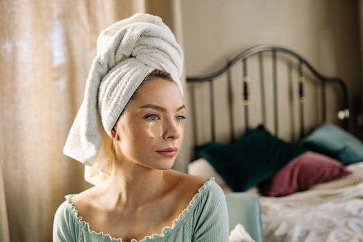 Woman practicing self-care with under eye patches and a towel on her head.