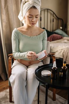 Pregnant woman in a relaxed posture applying skincare products with care.