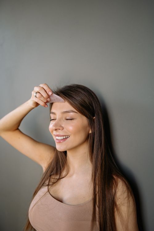Free Woman smiling while using a gua sha stone on her forehead, relaxing in her skincare routine. Stock Photo