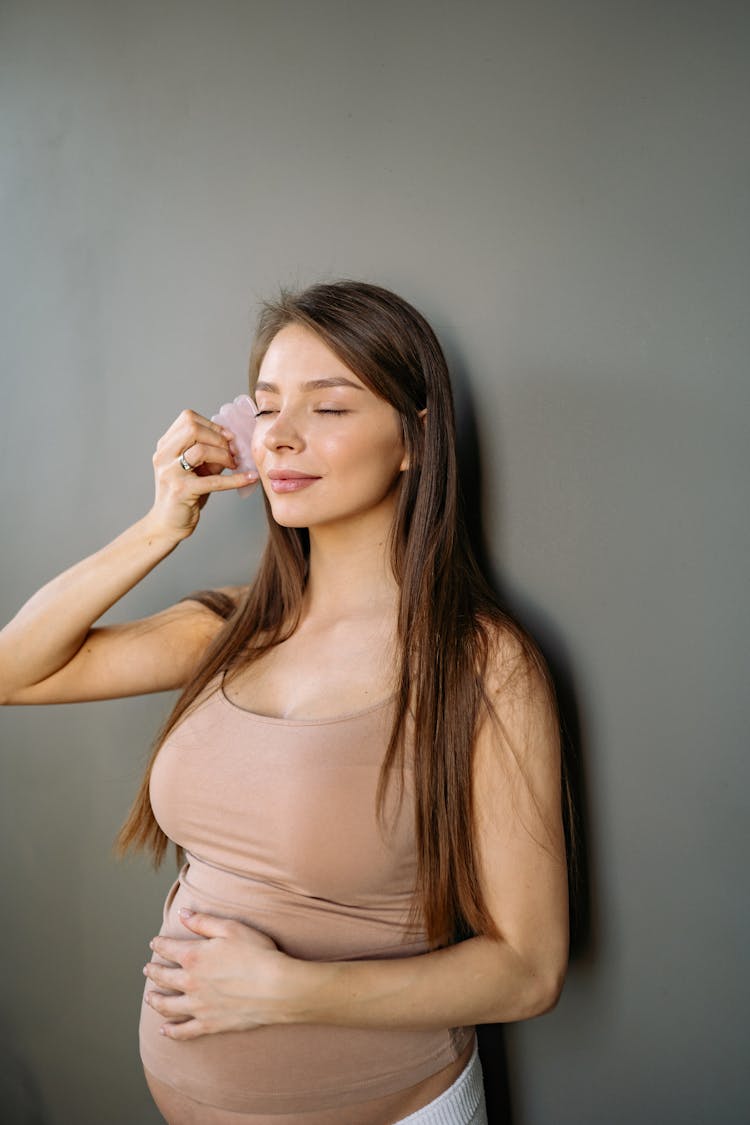 Pregnant Woman In Tank Top Holding A Piece Of Stone On To Her Face