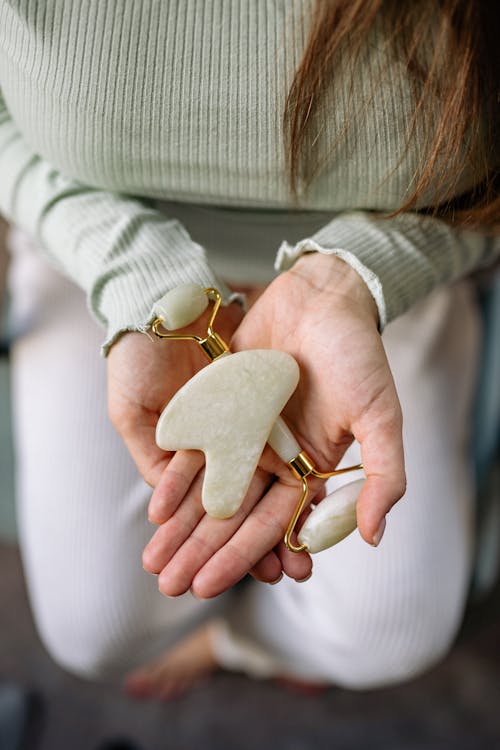 Person Holding a Stone Massager and Jade Roller