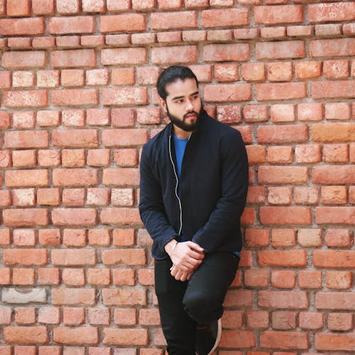 Free Young Man with Dark Hair and Beard Leaning Against a Brick Wall  Stock Photo
