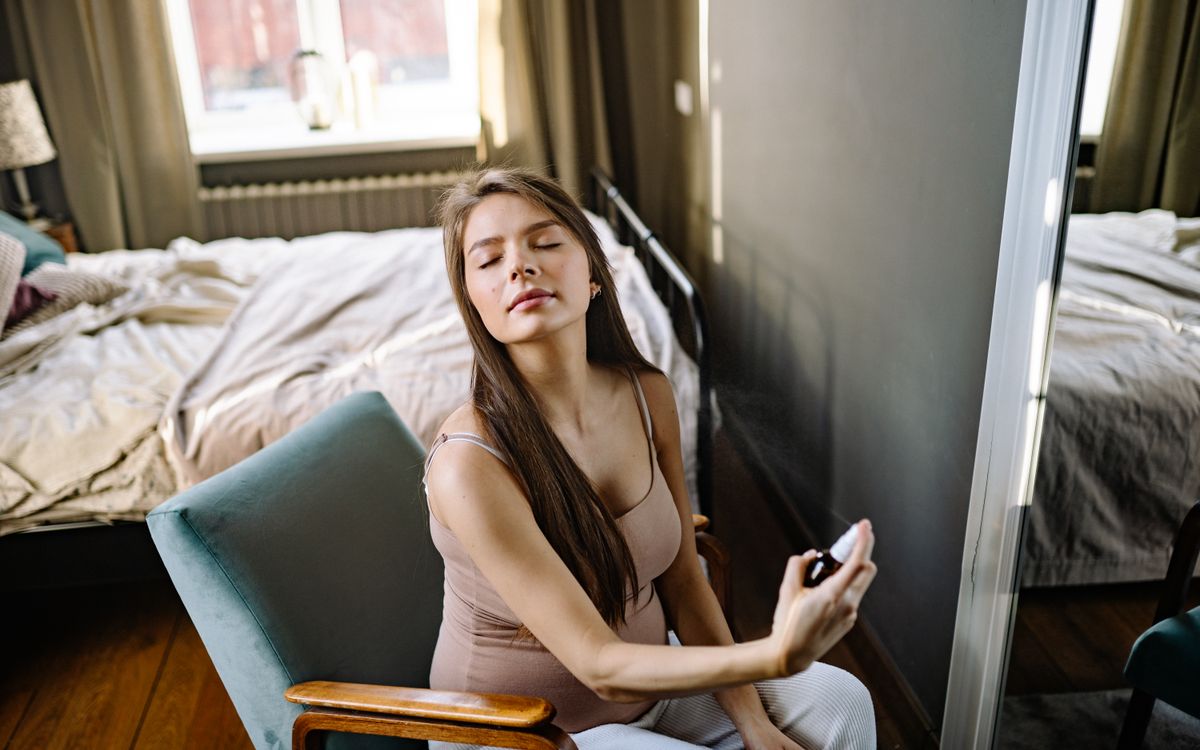 Pregnant woman sitting indoors, eyes closed, enjoying a refreshing fragrance.