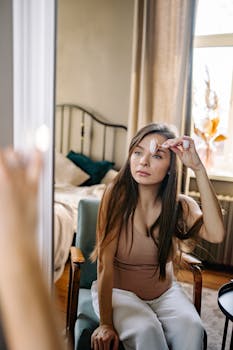Pregnant woman in a cozy bedroom using a face roller while sitting and looking in the mirror.