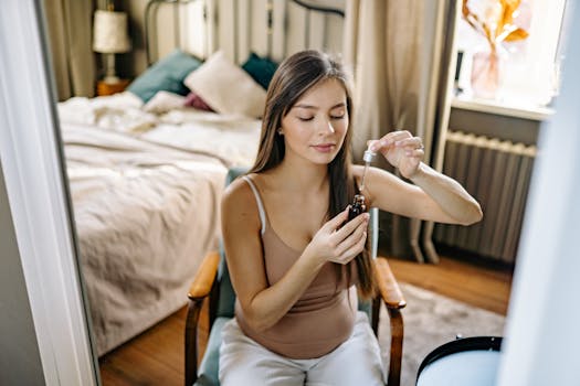 A woman in a tank top applies skincare serum while seated in a comfortable bedroom.