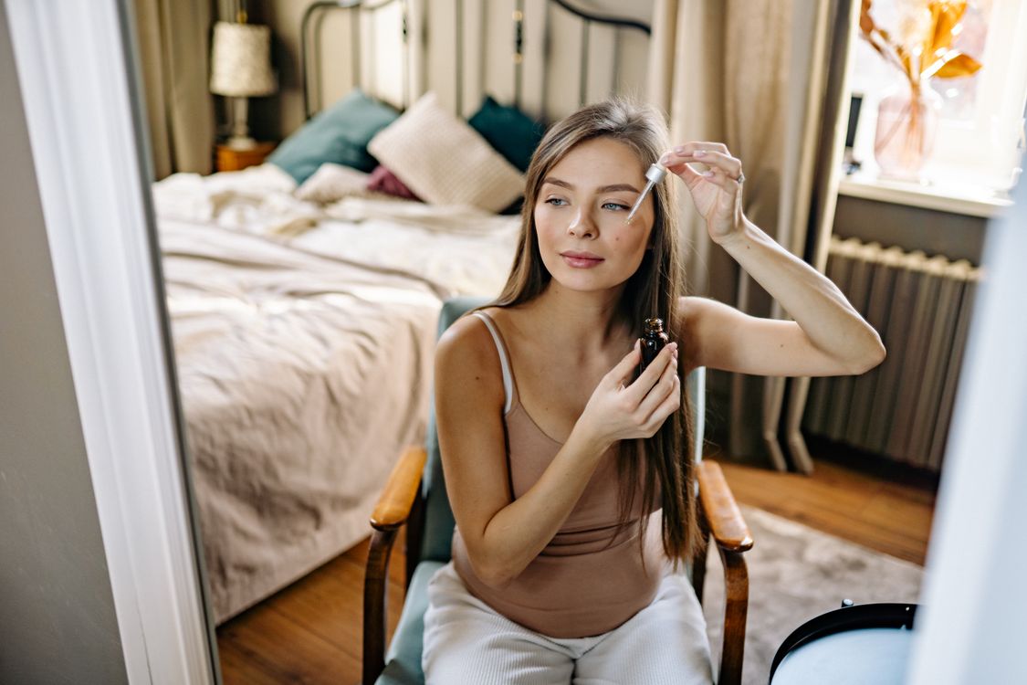 Free A woman using a dropper for skincare routine in a cozy bedroom setting. Stock Photo