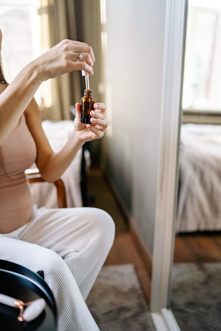 A Person Holding A Brown Bottle And A Dropper