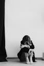Full body of black and white unrecognizable depressed female covering face while embracing knees sitting on floor