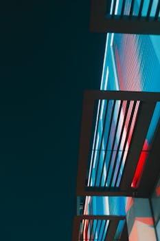 Low angle view of a modern building facade illuminated with colorful LED lights against a dark sky.