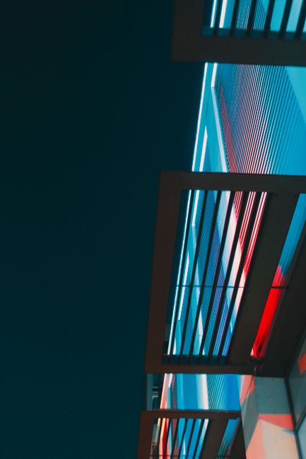 Low angle view of a modern building facade illuminated with colorful LED lights against a dark sky.