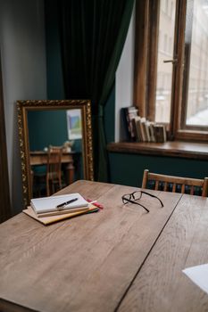 A cozy indoor workspace with eyeglasses, a notebook, and a pen on a wooden table.
