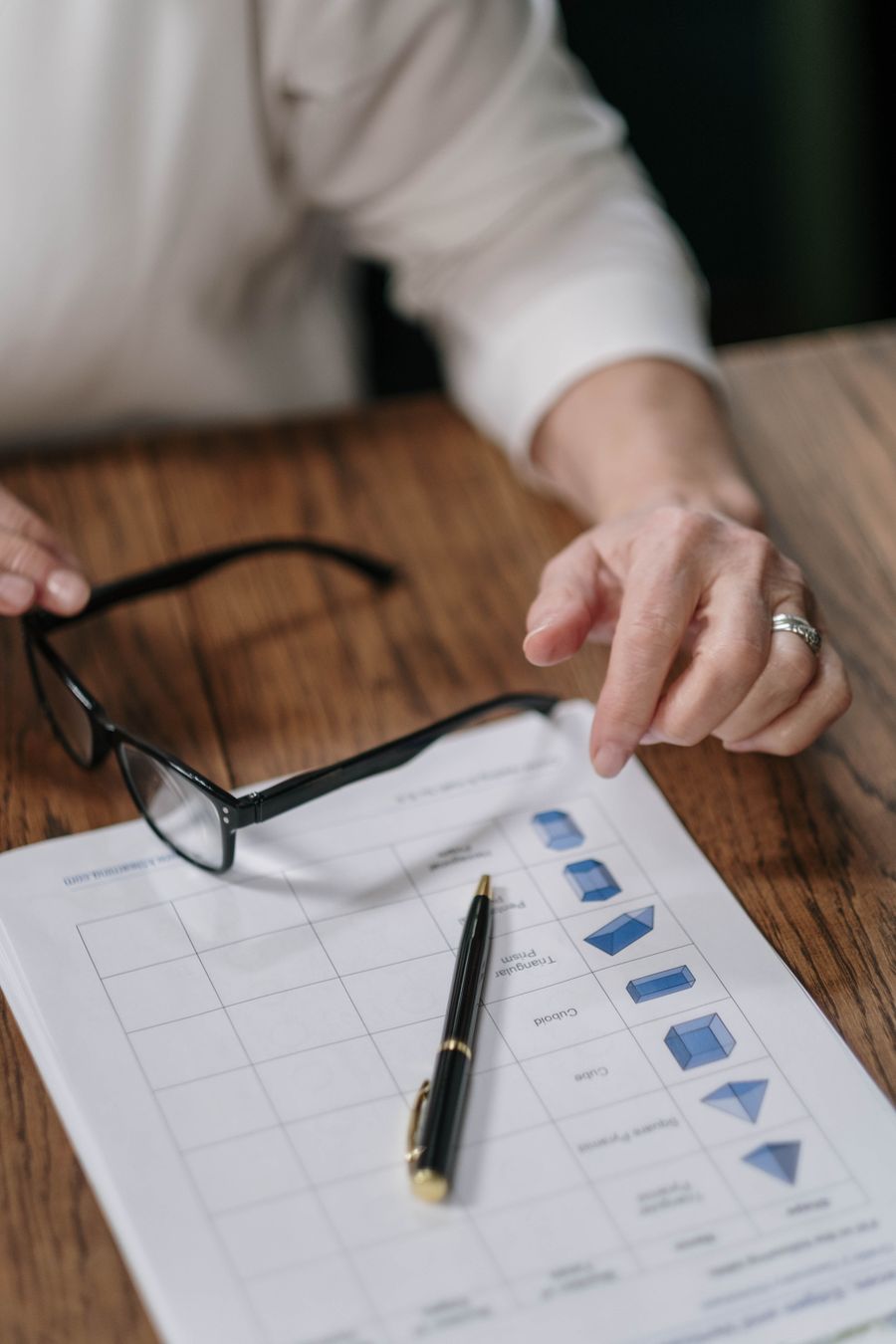 A person reviews paperwork with a pen and glasses on a wooden surface, emphasizing business analysis.