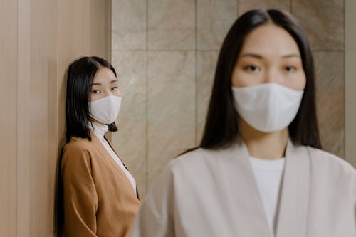 A Woman Wearing White Face Mask Leaning on Brown Wall