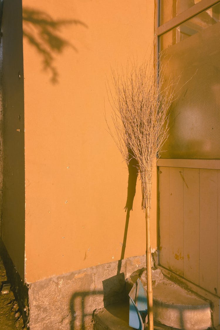 Broom Stick Leaning In A Yellow Wall 