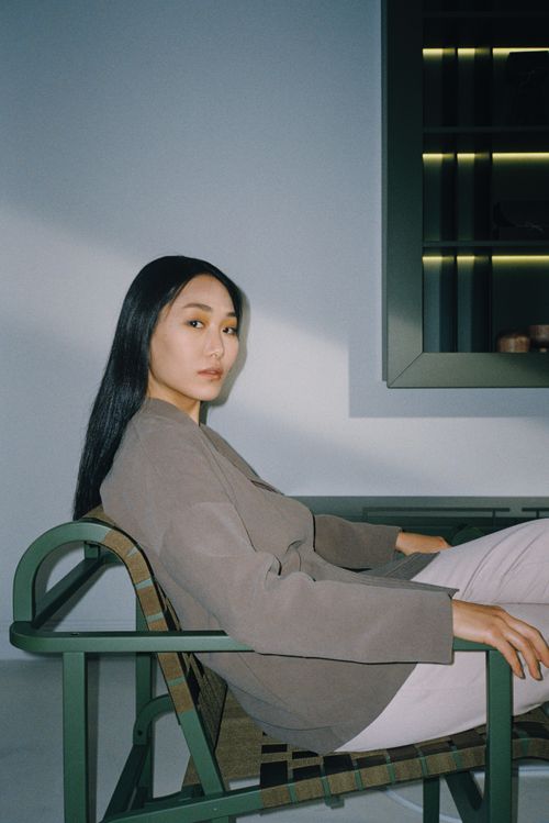 Free Portrait of a poised Asian woman seated indoors with a modern fashion aesthetic. Stock Photo