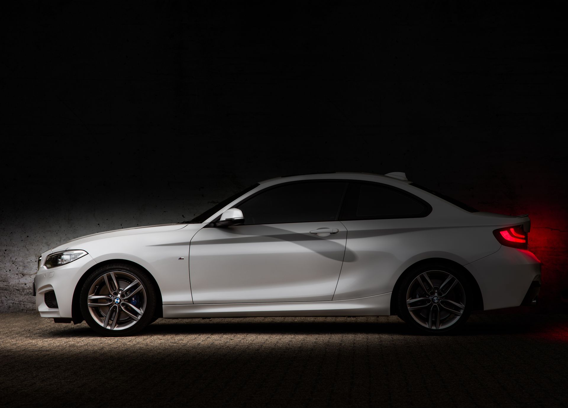 Side view of a white BMW 220D parked in a dark area, showcasing luxury design.