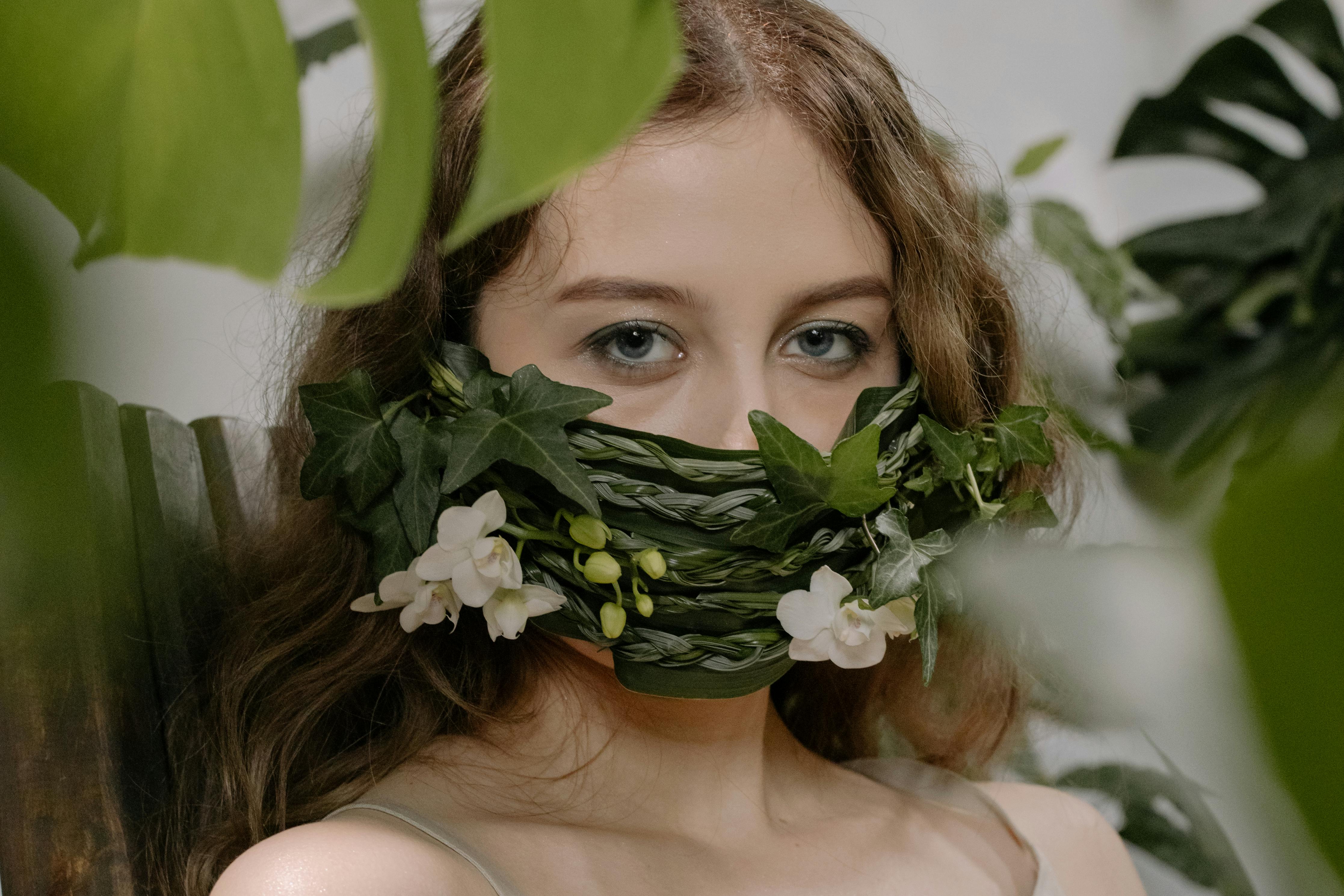 A creative portrait of a woman wearing a nature-inspired face mask made of ivy and orchids.