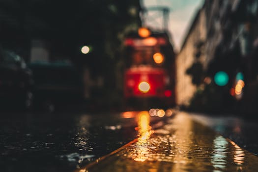 A moody, blurry shot of an urban street reflecting lights with a tram in the background.