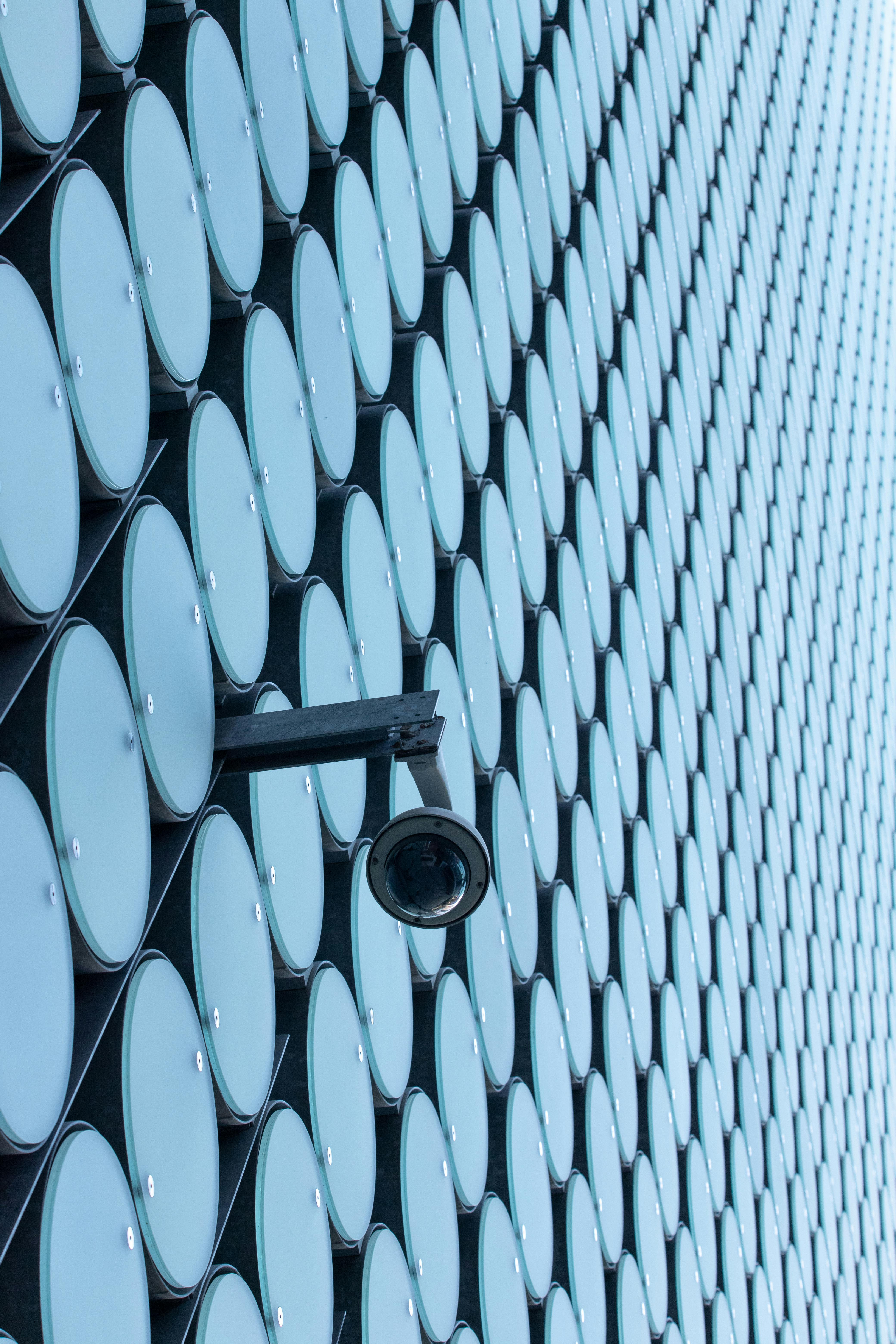 A modern building facade featuring repetitive circular patterns with a security camera.
