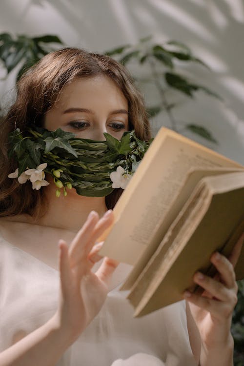 Free Photograph of a Woman Reading a Book with Leaves on Her Face Stock Photo