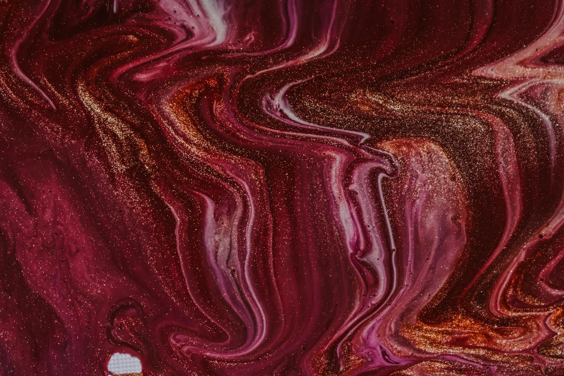 Top view of abstract background of mixed wet white and fuchsia paints with golden sequins spilled on surface