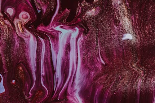 Bright wet purple dye with golden sequins spilled on surface with white paint and forming abstract background