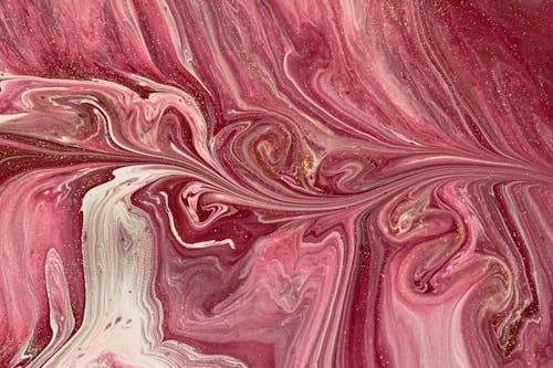 From above closeup of swirling pattern created by liquid pink paint with glossy surface as abstract background