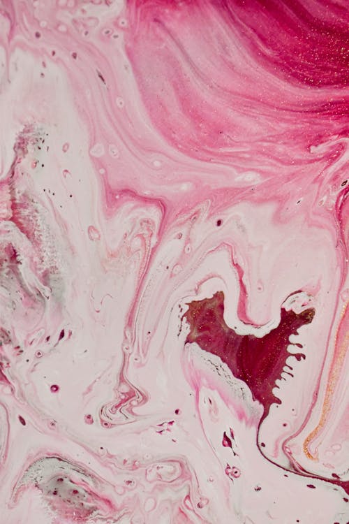 From above surface of liquid white paint with bright red and pink stains as abstract background