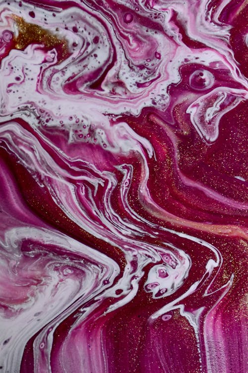 Top view closeup of bright fuchsia and white liquid paints mixing chaotically and forming creative pattern