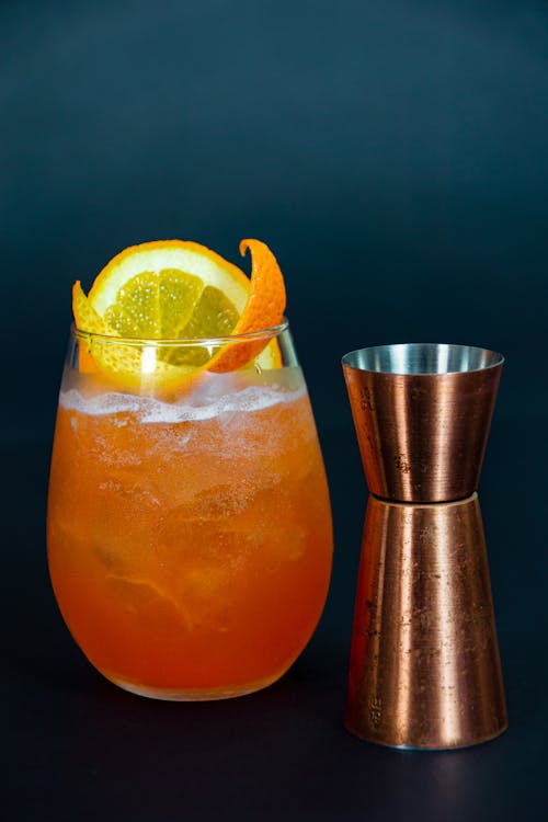 Free Close-Up Photo of an Orange Drink Beside a Copper Shot Glass Stock Photo