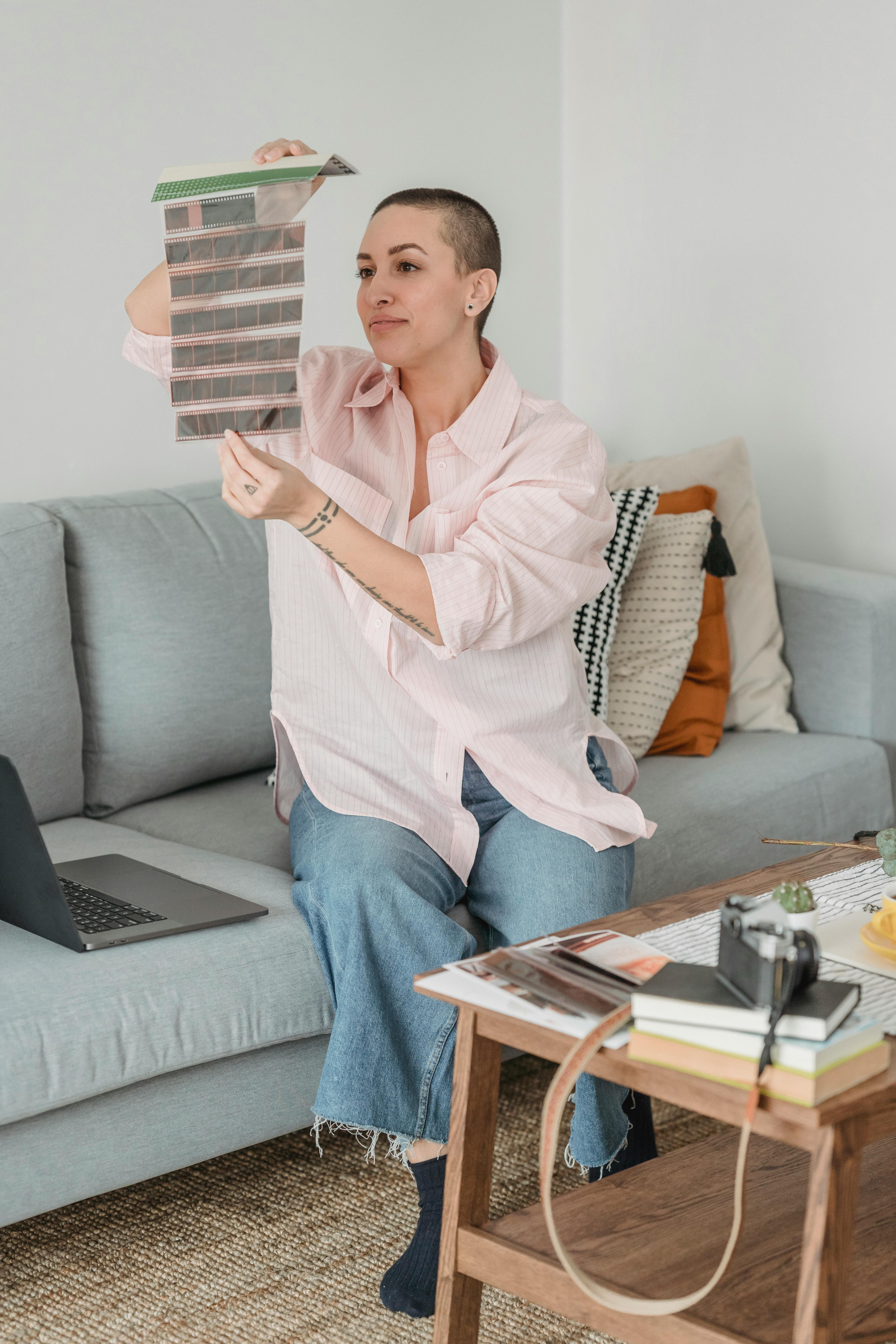 young woman examining film strips sitting on sofa in modern apartment