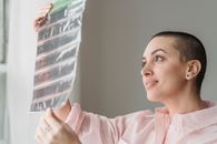 Side view of positive young female photographer watching filmstrip and smiling standing near window in light studio